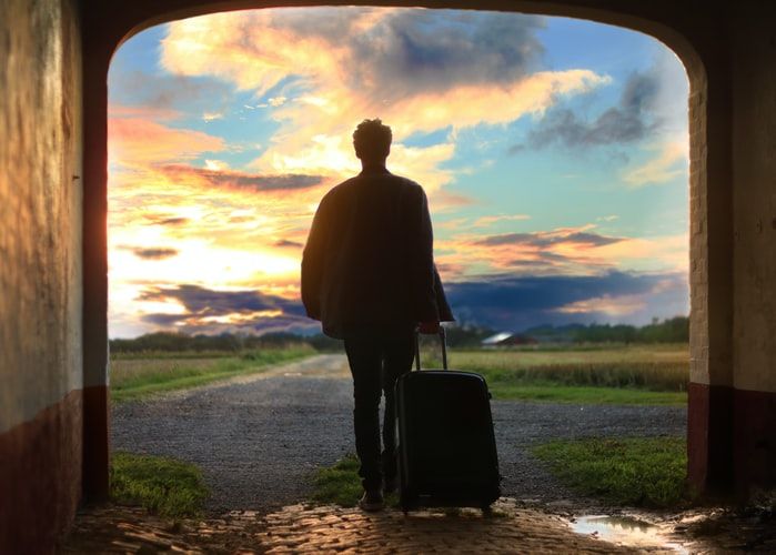Man walking into sunset with suitcase