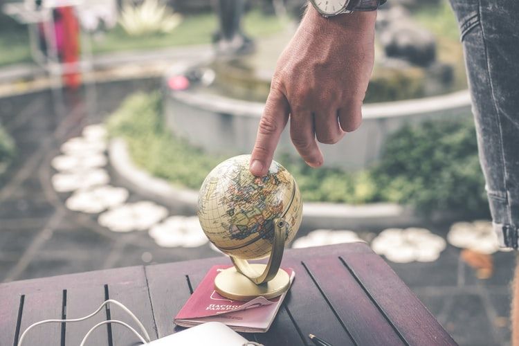Hand pointing to a spot on a mini world globe