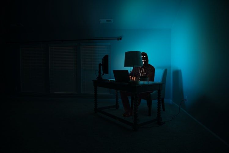 Masked person using computer in darkened room
