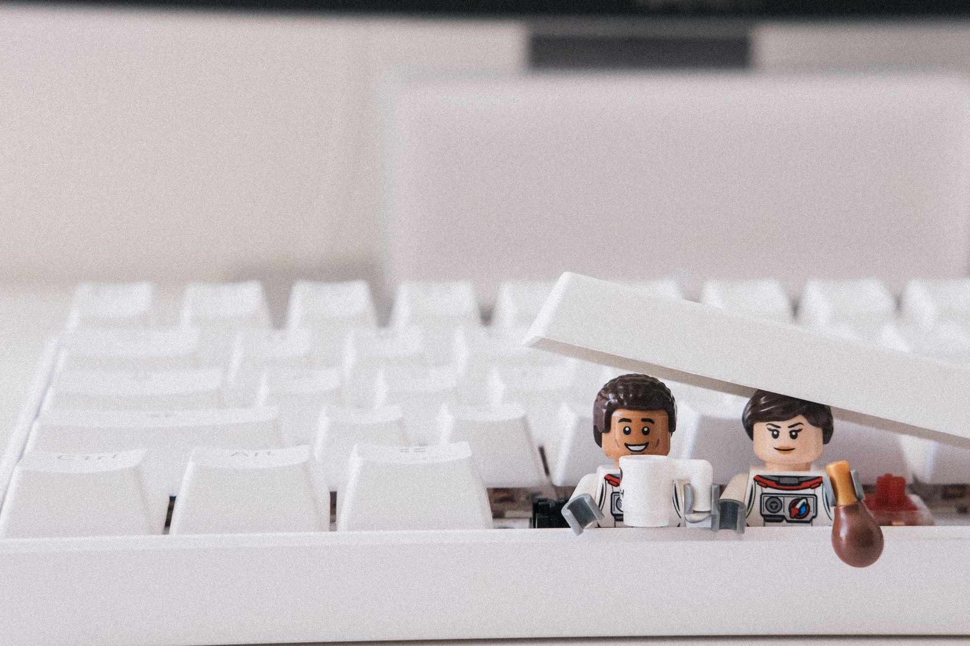 Two Lego people popping put from under a computer keyboard's keys