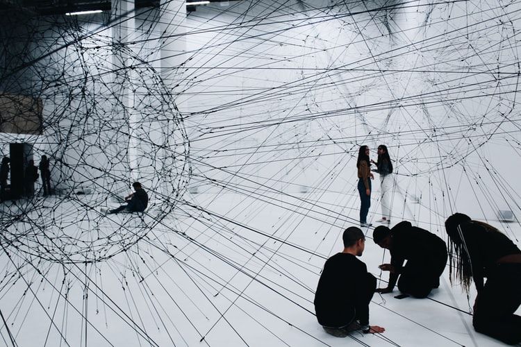 People wearing black in a white room with black art installation