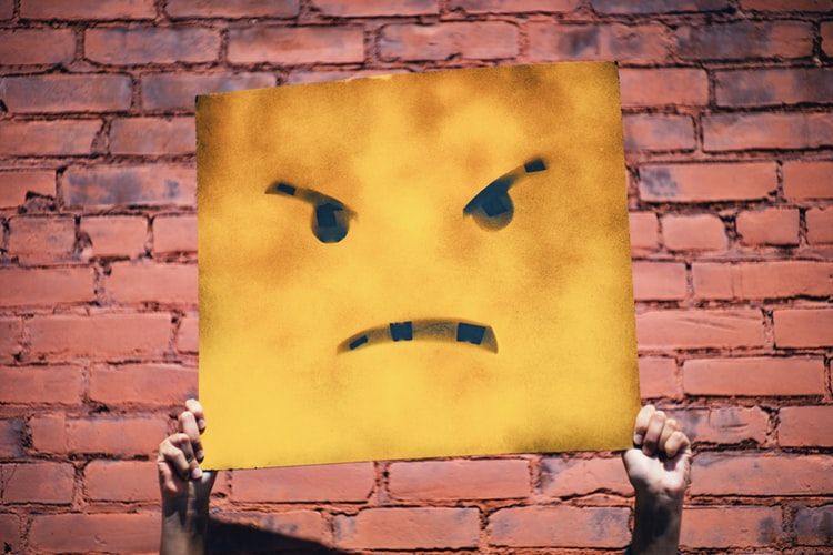 Person holding up sign with angry face on it
