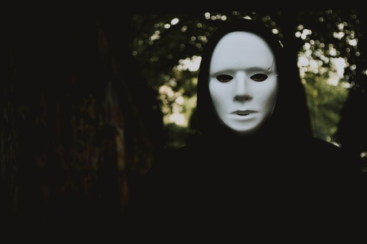 Person wearing a cloak and white face mask