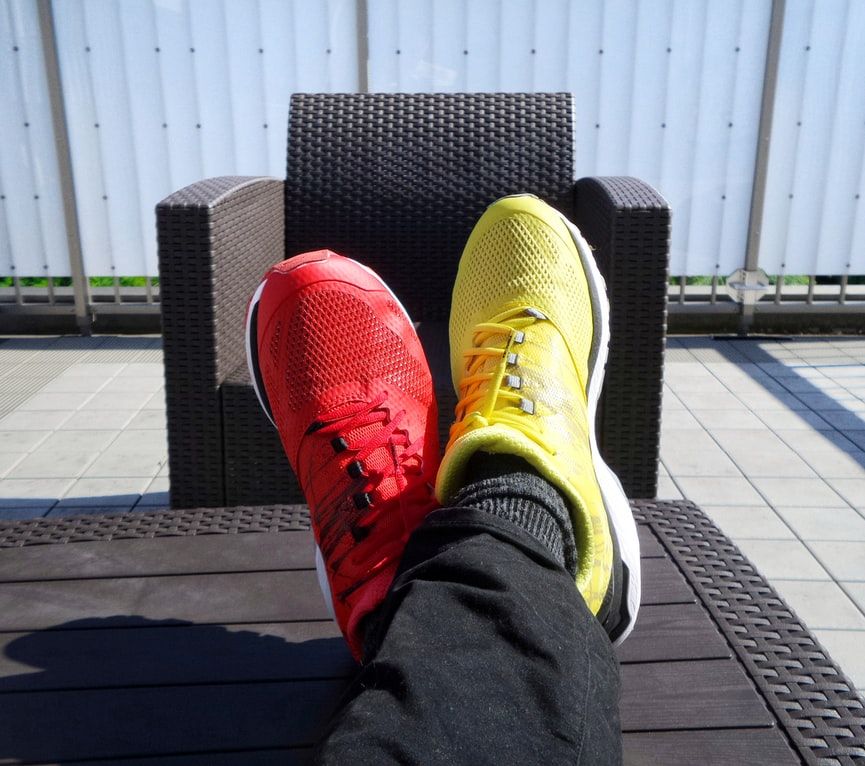 Person wearing one red sneaker and one yellow sneaker with their feet up on a table