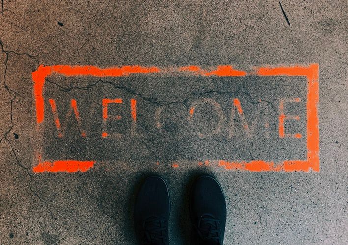 Feet standing in front of a spray painted sign on the ground saying 'welcome'