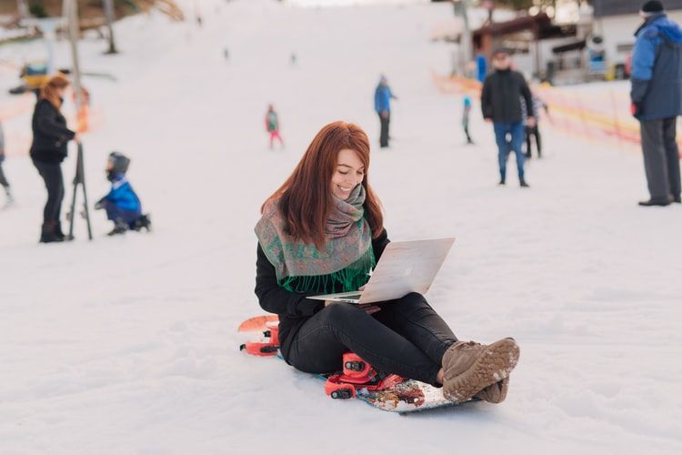Woman sitting on a ski slope using her laptop and smiling