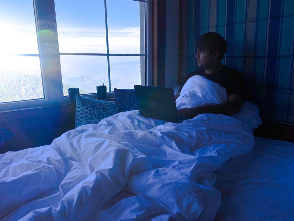 Man using laptop in bed in the early morning 