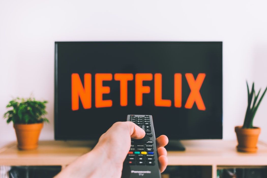 Netflix logo on a TV screen with hand holding a remote control