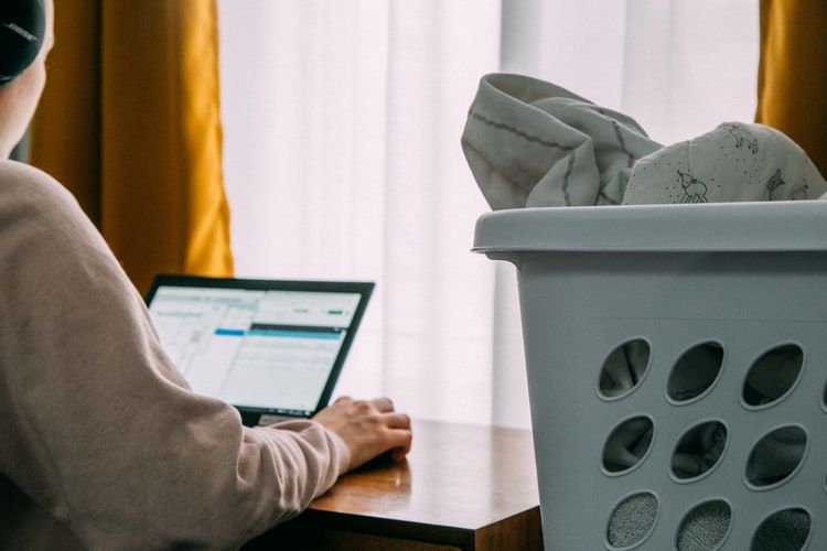Person using a laptop next to a laundry basket of clothes