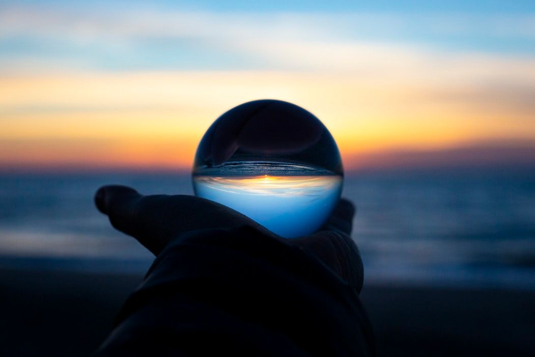 Hand holding a globe in front of the ocean at sunset