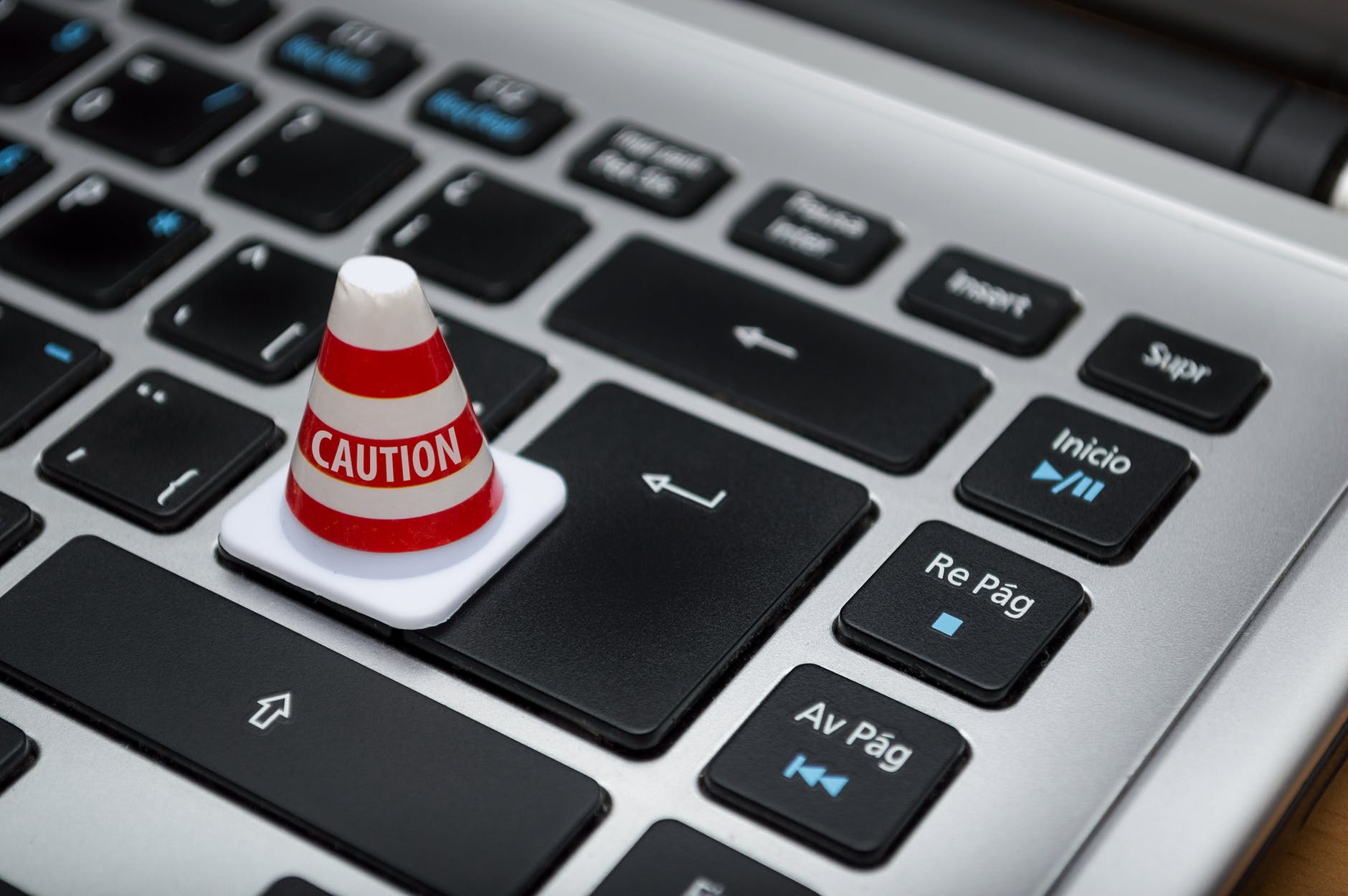 Mini traffic cone with the word caution on it standing on a computer keyboard