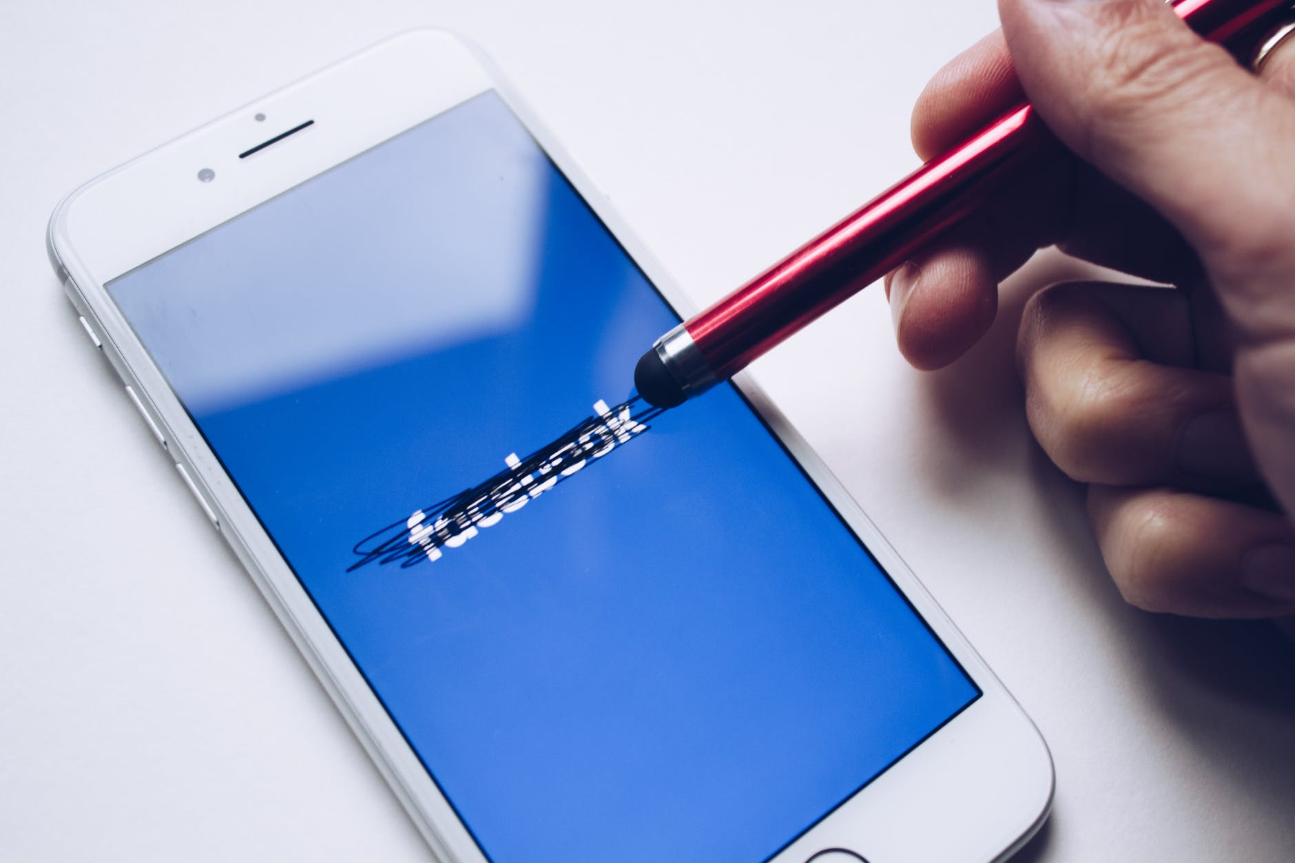 Person crossing out the Facebook logo on their phone with a pencil eraser