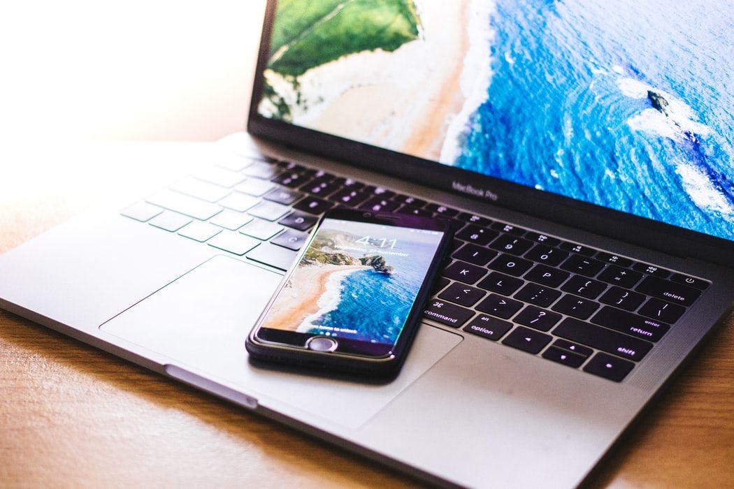 A phone and laptop with identical ocean and shoreline wallpapers