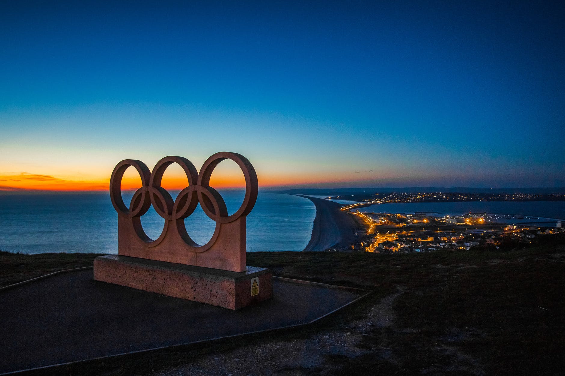 A sculpture on the Olympic rings overlooking a port at night