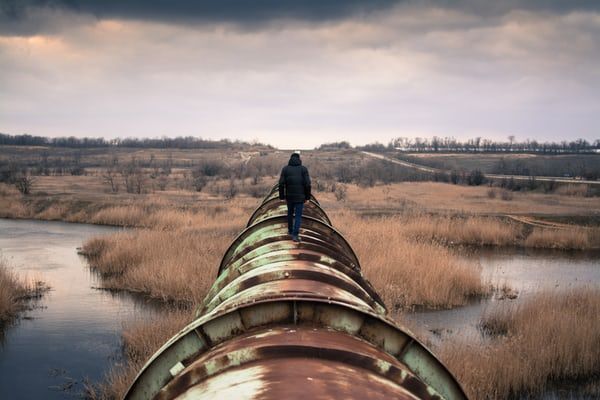 Hooded person walking on top of a pipeline