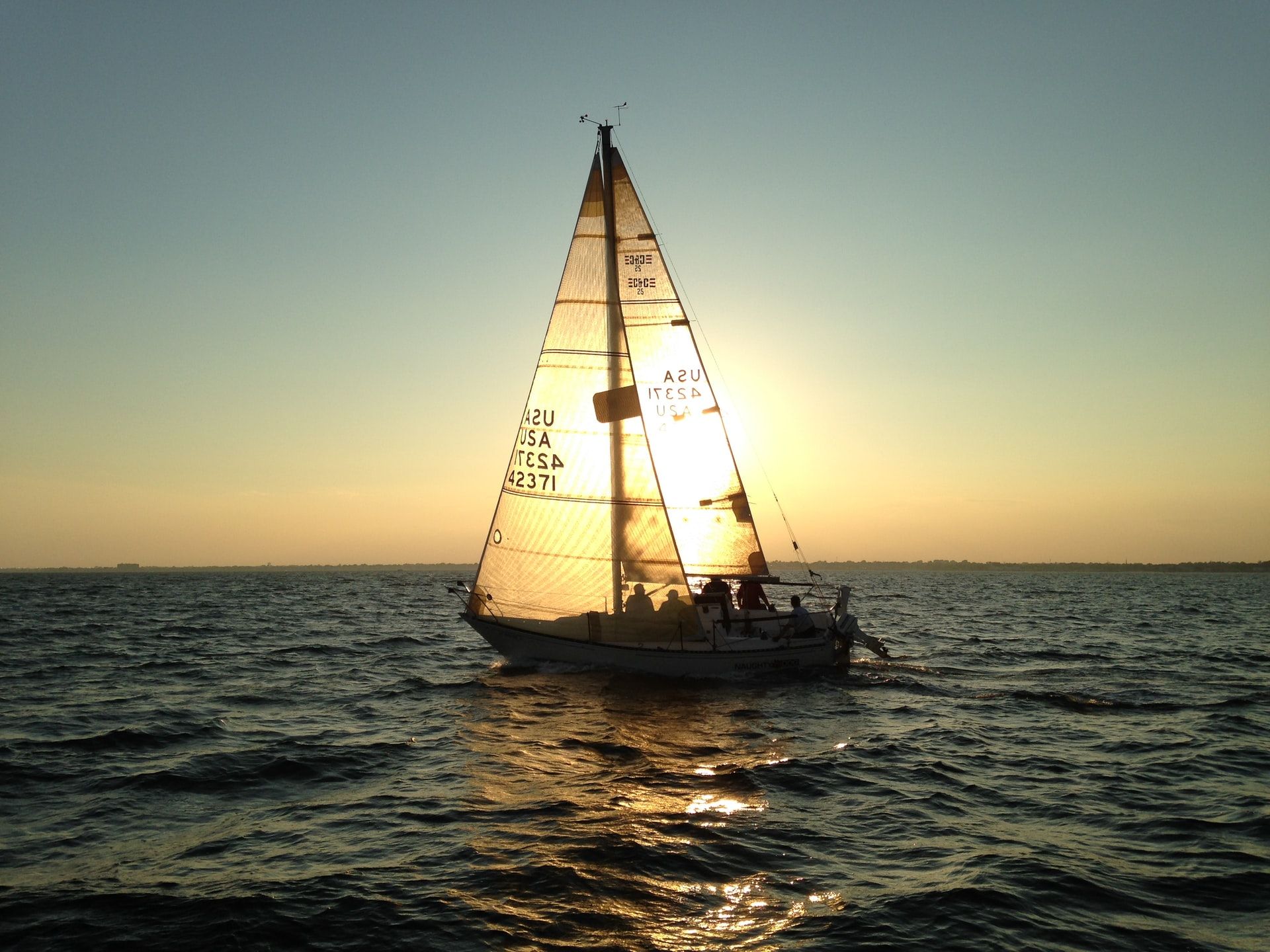 Small sailing yacht with the setting sun glowing through its sails