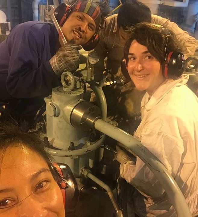 Smiling seafarers working on an engine while one takes a selfie