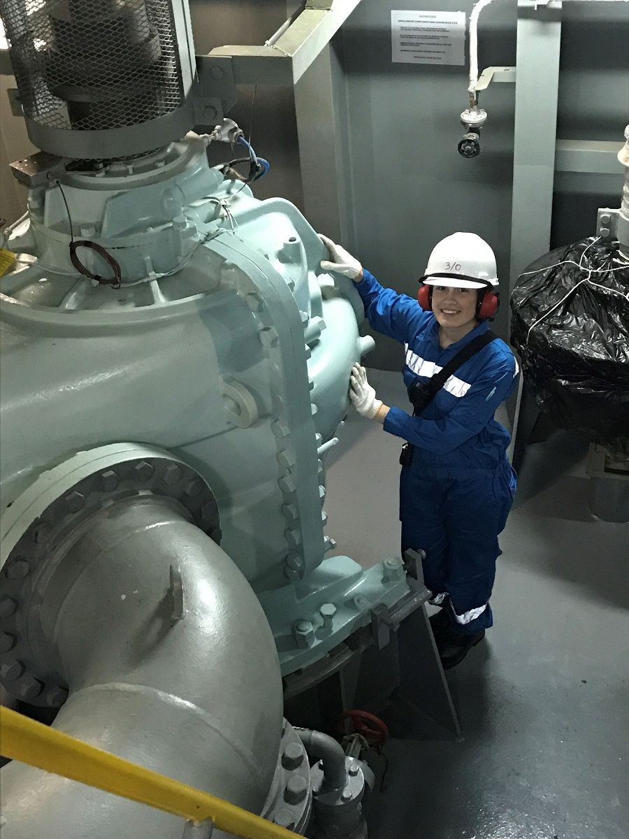 Smiling female engineer dwarfed by a huge piece f machinery on a ship