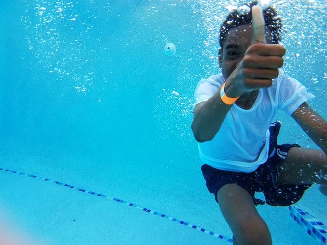 Man underwater in a swimming pool giving a thumbs up
