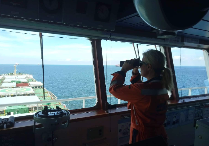 Seafarer looking out from the bridge of a ship through binoculars