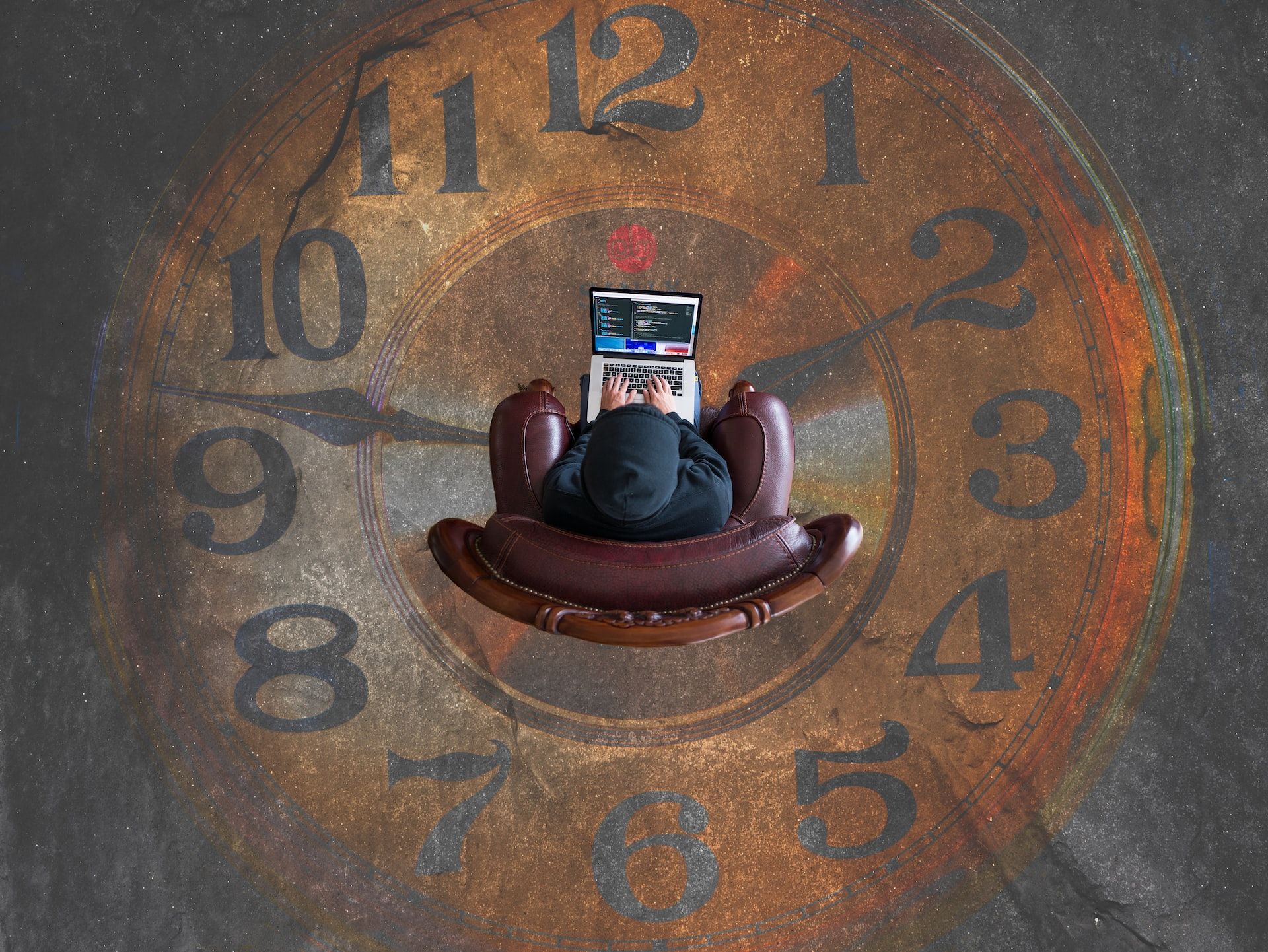 Person sitting on leather chair in the middle of a clock on the floor using a laptop