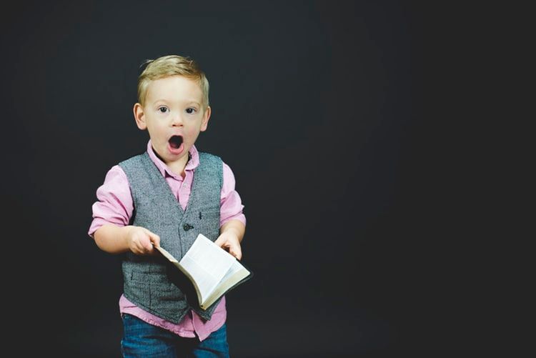 Little boy holding an open book and looking shocked