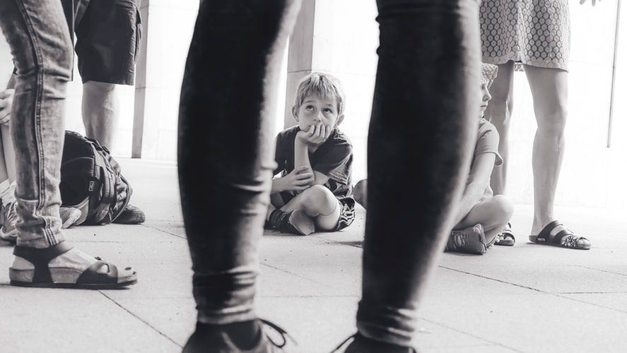 Child sitting on floor looking up at adults' legs