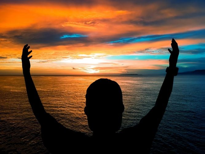Person raising their arms in front of the ocean at dusk