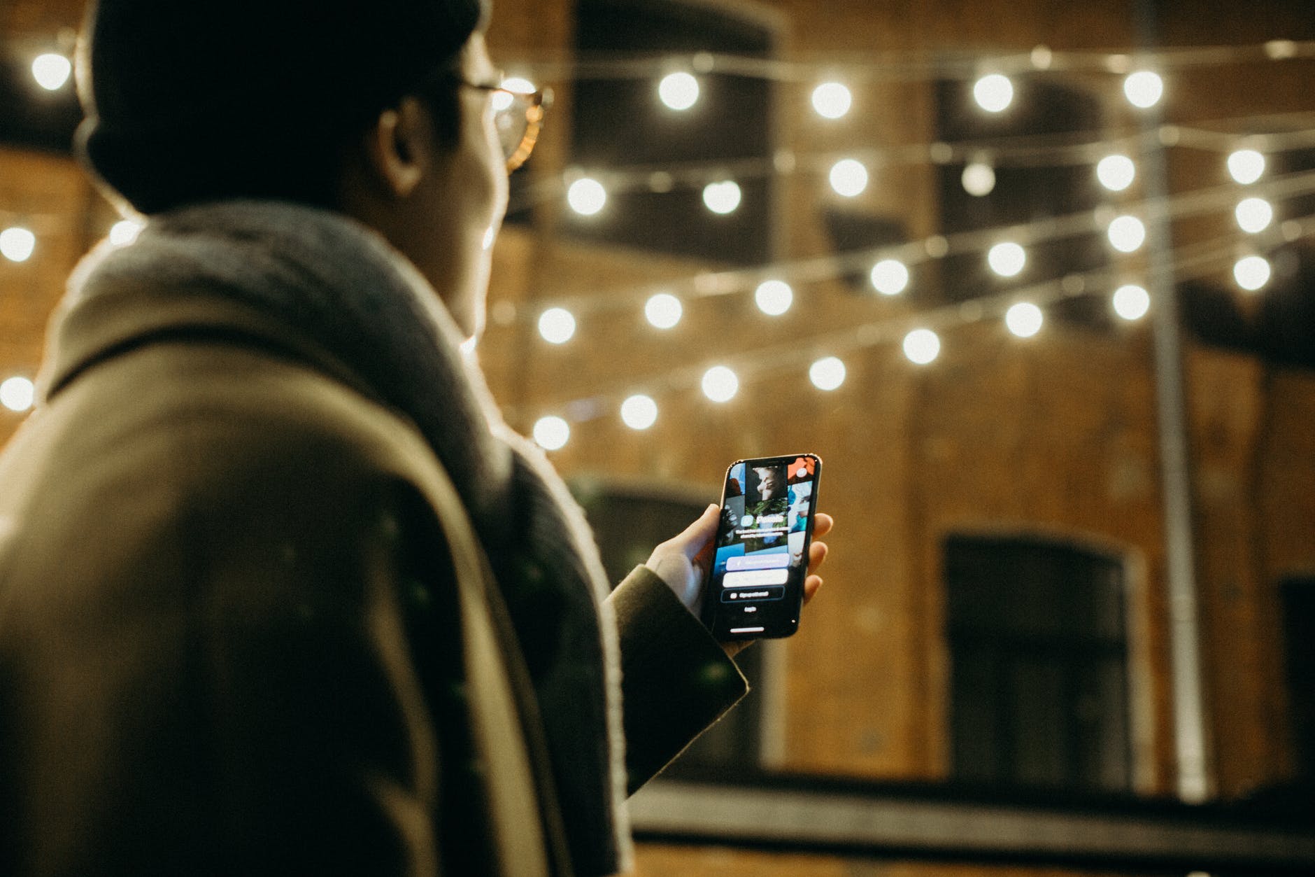 Man standing under a string of fairy lights looking at their phone