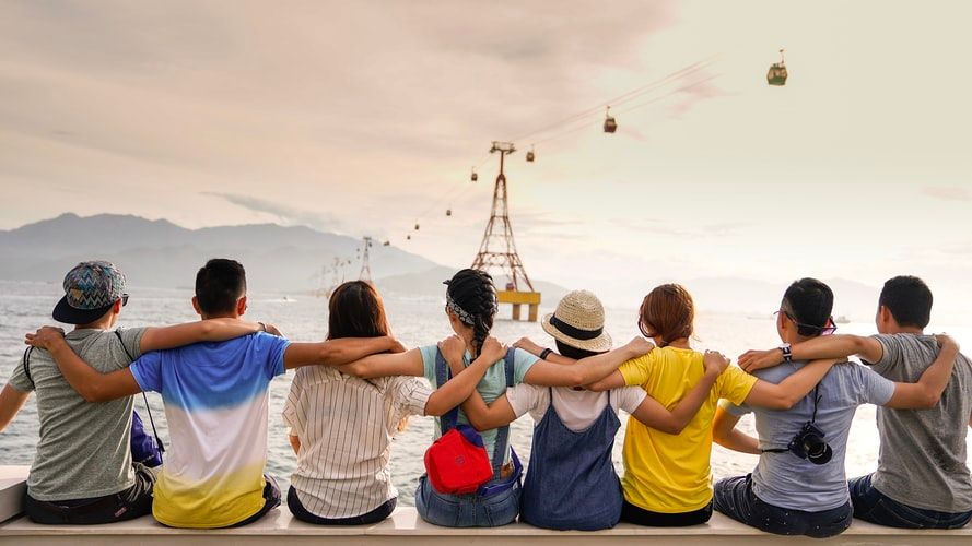 Group of friends with arms around each other's shoulders looking at the sea