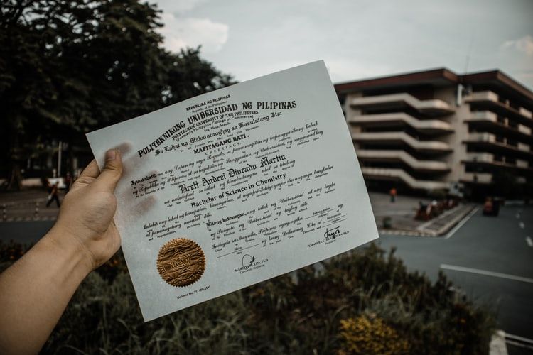 Hand holding certificate in front of a university building