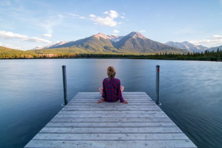 Person sitting alone on a dock looking at a lake and mountains