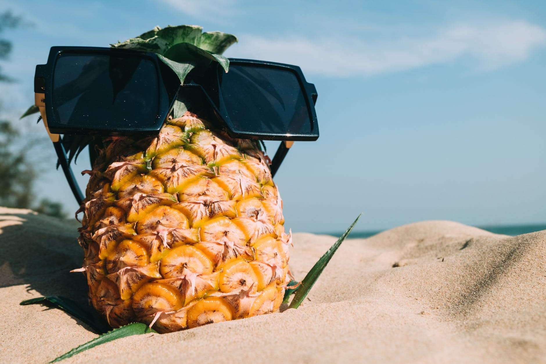 A pineapple on a beach wearing sunglasses