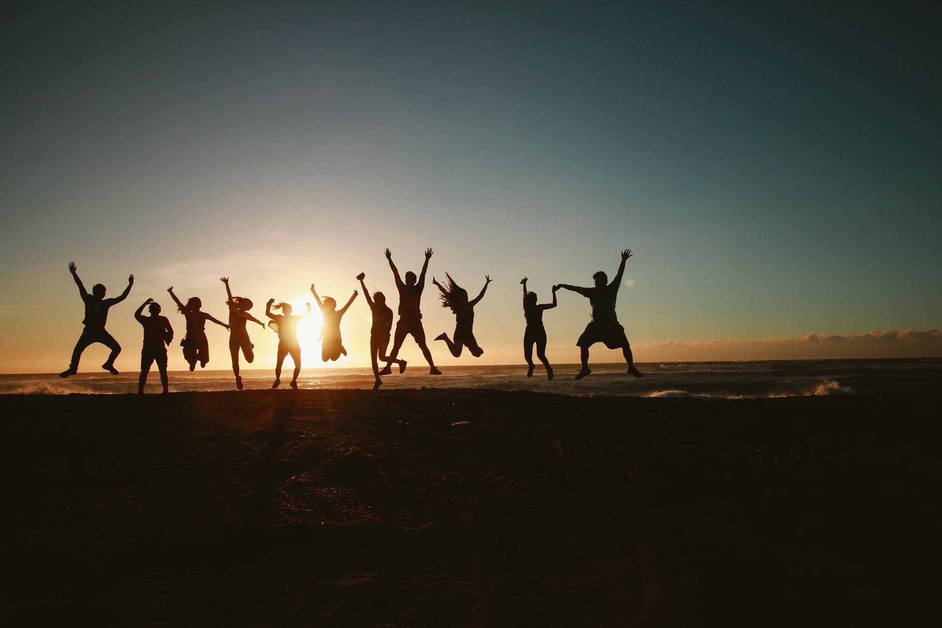 Group of people jumping into the air on a beach at sundown
