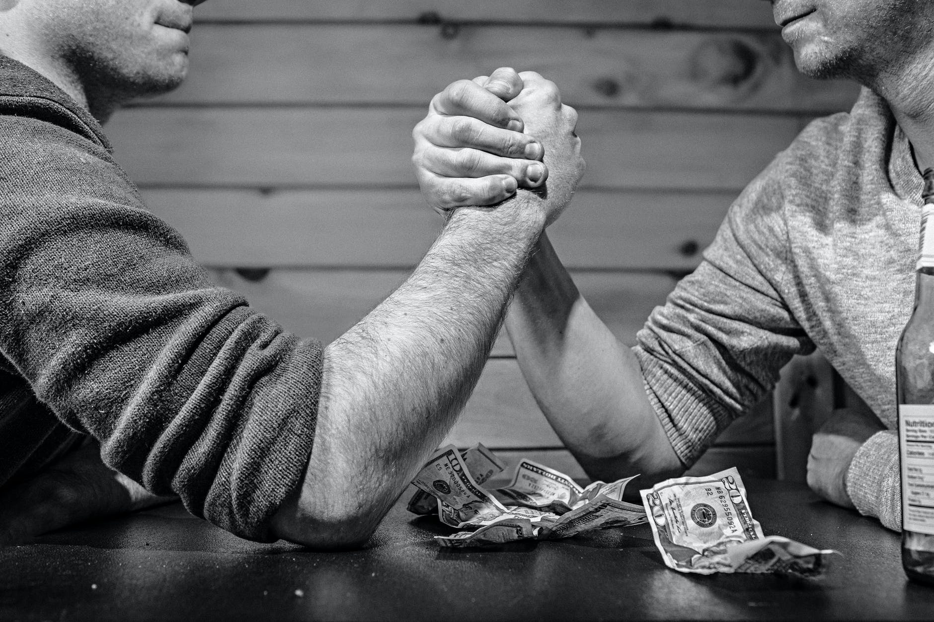 Men arm wresting over a pile of dollar bills