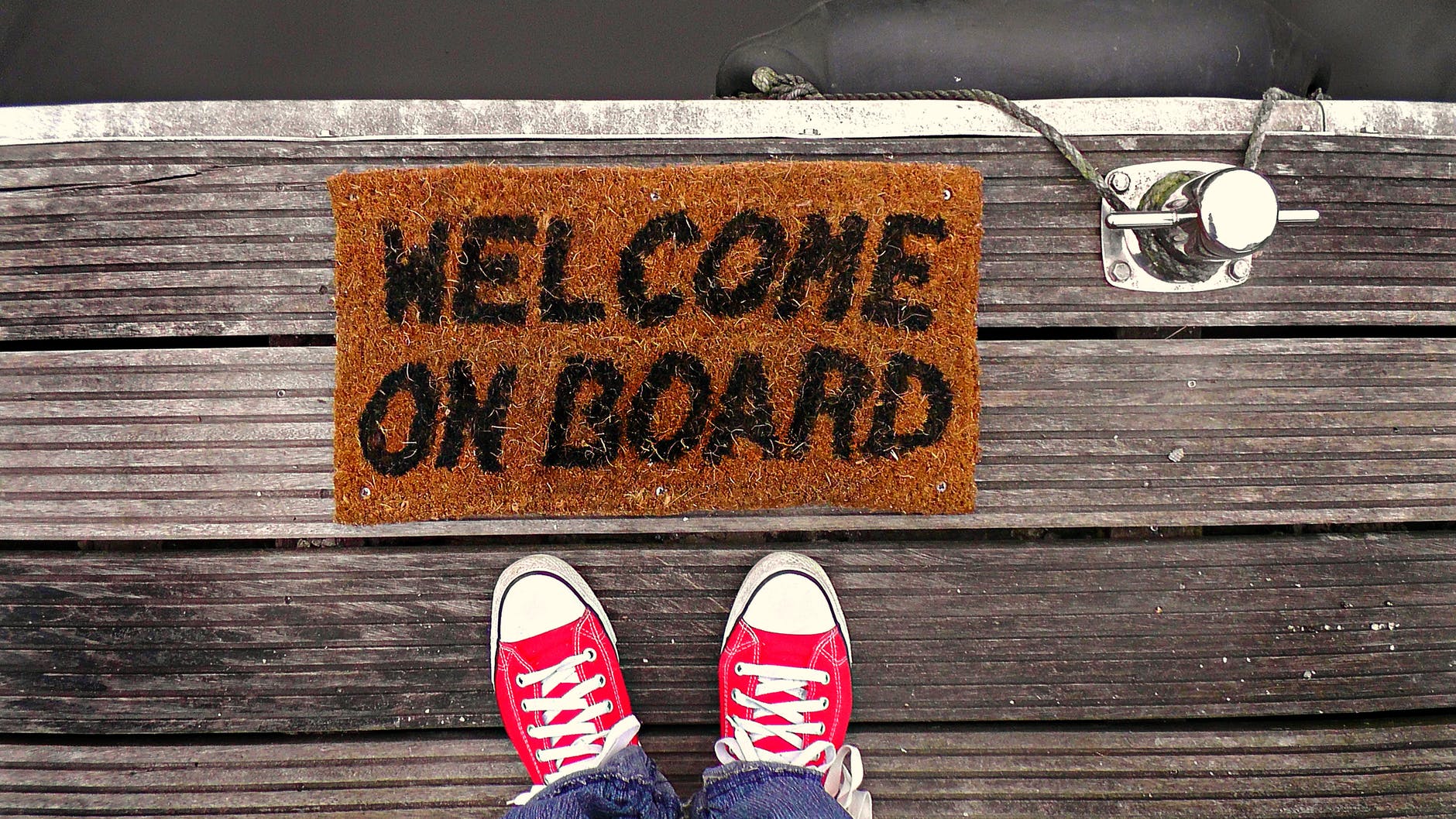 Feet standing next to a doormat on a dock that says 'welcome on board'