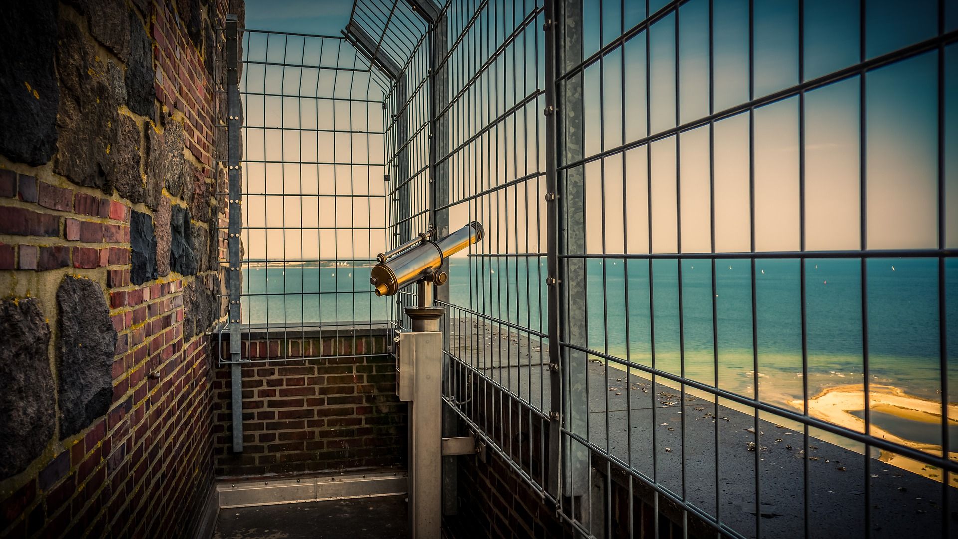 Telescope behind a wire grill pointing at the ocean