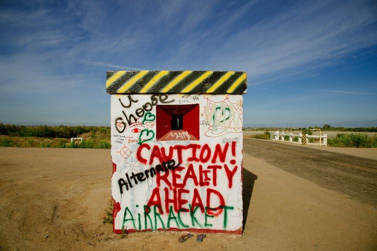 Structure covered in graffiti including wording saying 'caution reality ahead' 