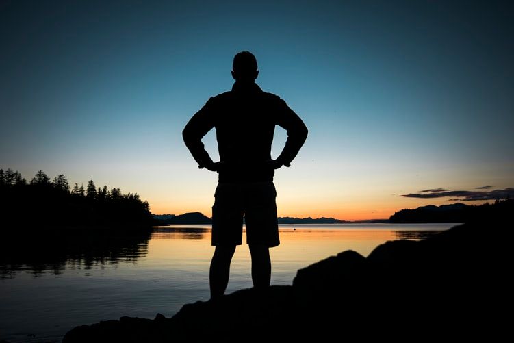 Silhouette of a man looking at water at sunset