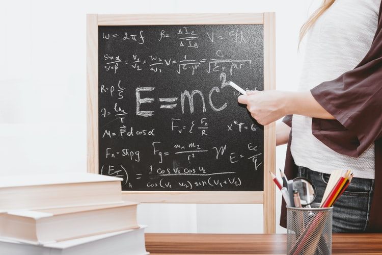 Teacher pointing to a chalkboard with equations written on it