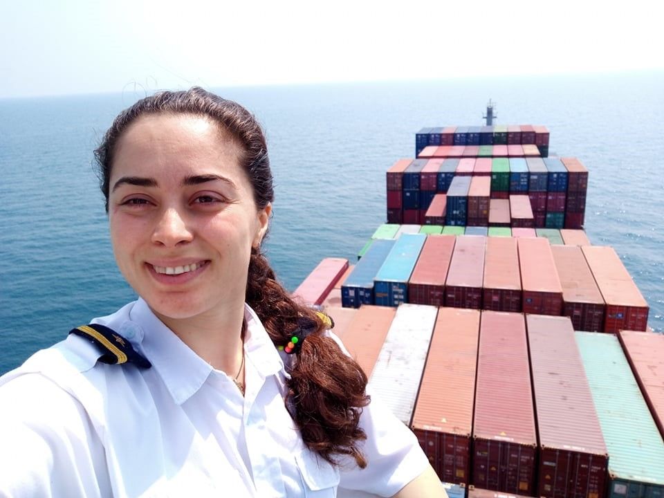 Smiling female officer taking a selfie on the deck of a container ship