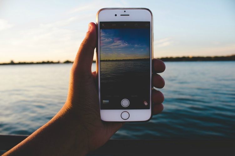 Hand holding a phone with the camera app open in front of a body of water