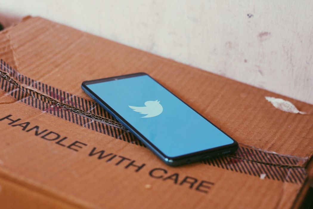 The Twitter logo on a phone resting on a carton that says handle with care