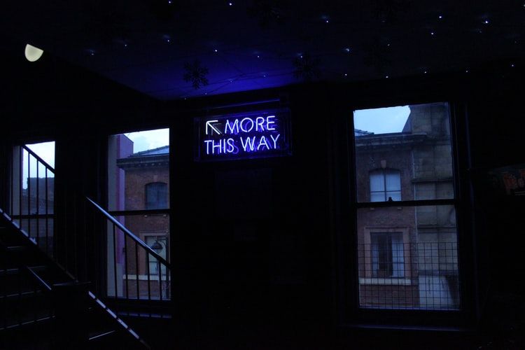 Neon sign pointing upstairs saying 'more this way'