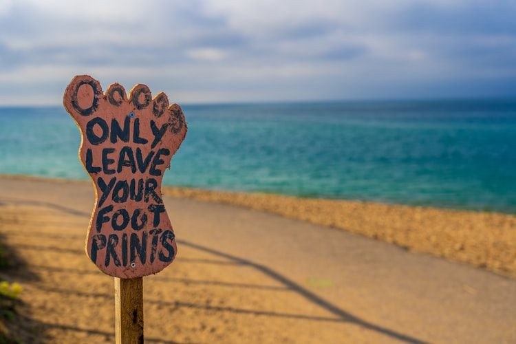Foot-shaped sign on a beach saying 'only leave your footprints'