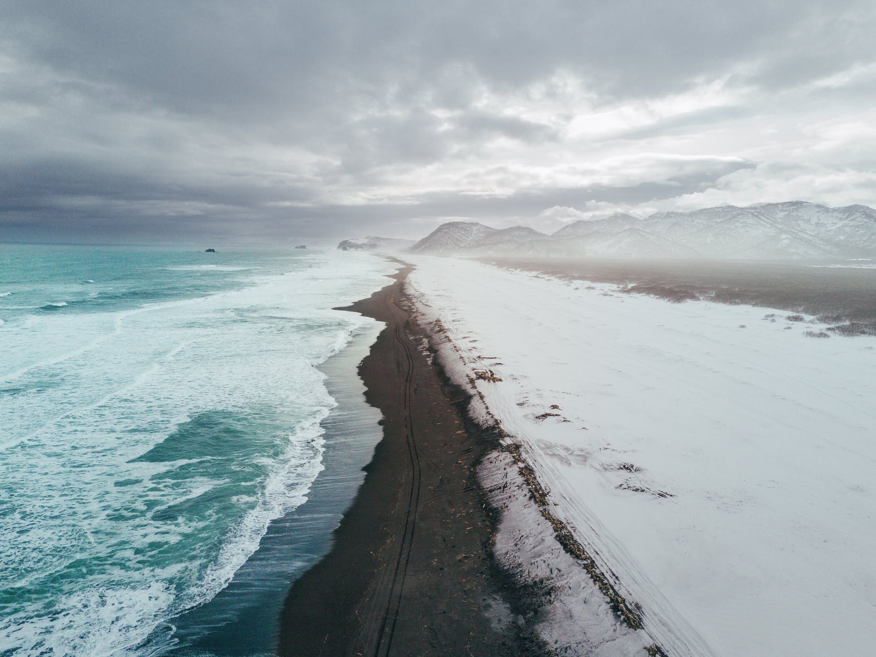 Thin strip of beach with ocean on one side and snow on the other