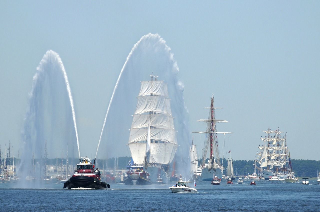 A fireboat spraying water to welcome sailing ships into harbor