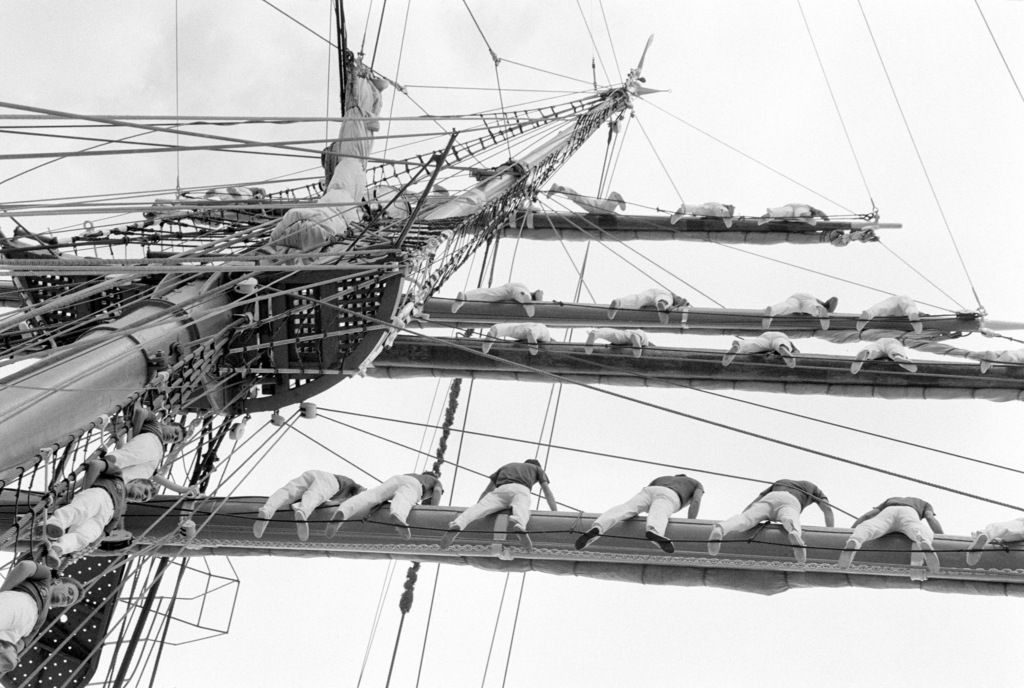 Black and white photo of sailors in the rigging of a sailing ship