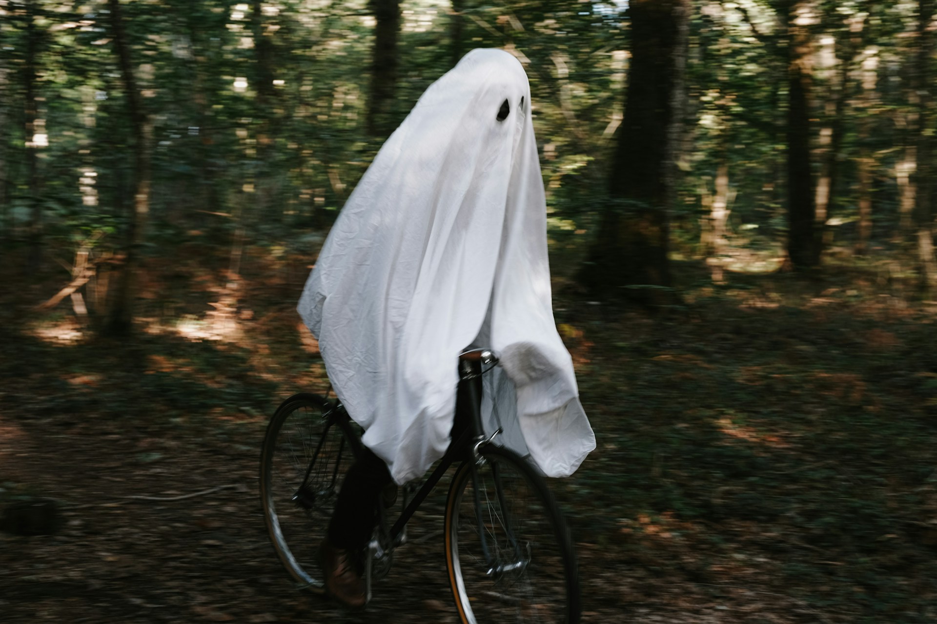 a person in a ghost costume riding a bike through some woods