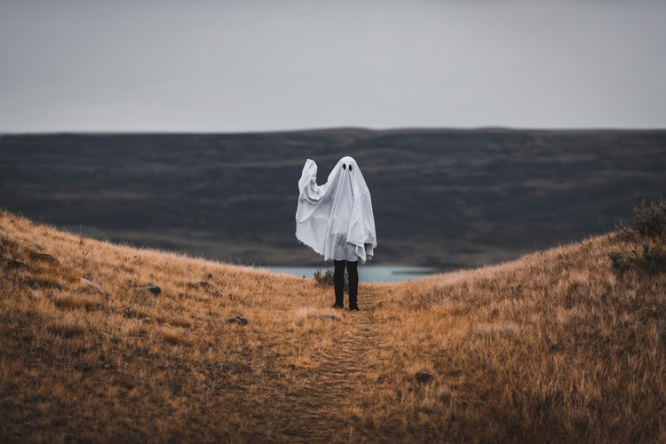 Person dressed as a ghost standing on a cliff and waving 